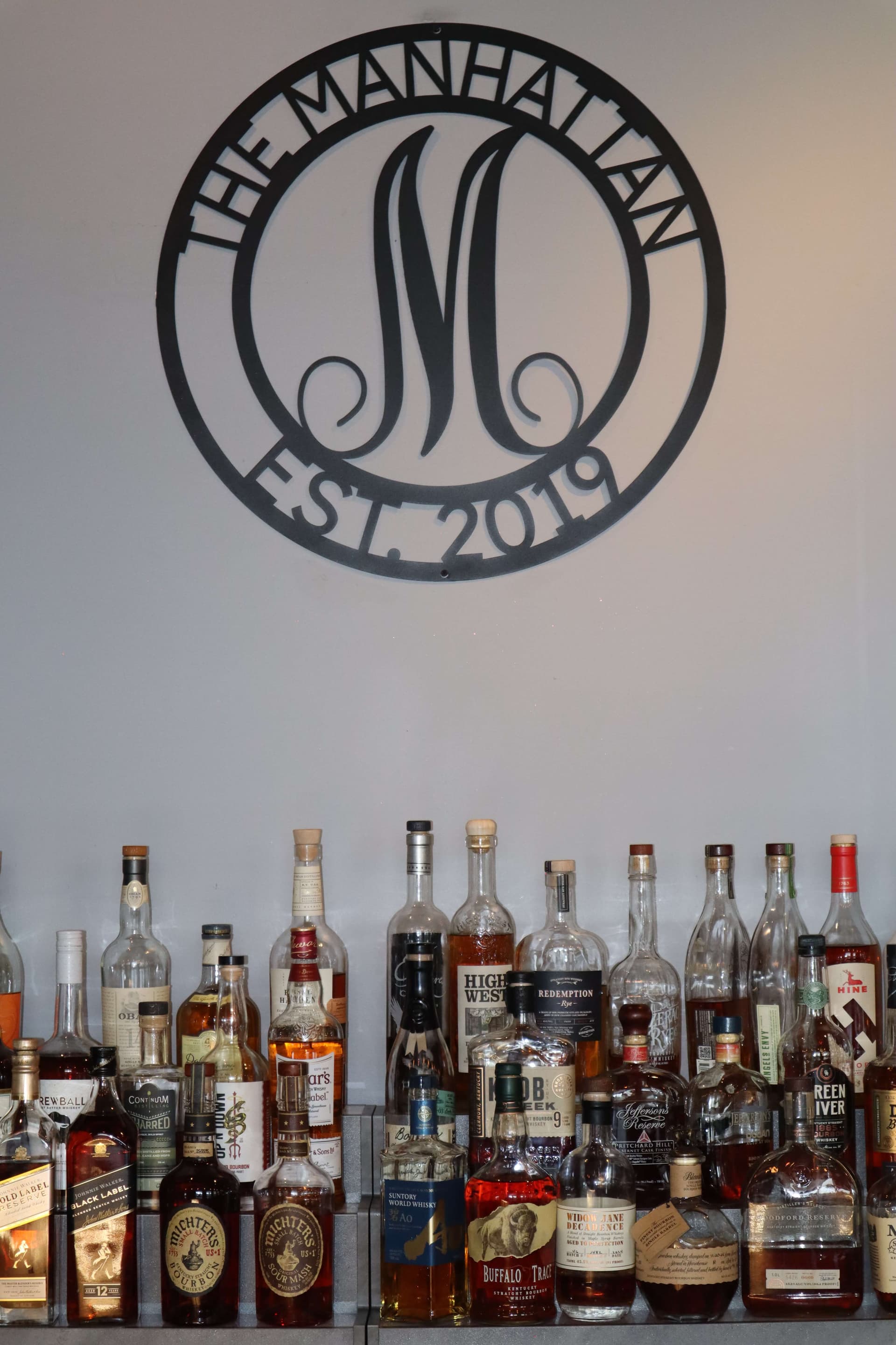 The Manhattan Est. 2019 emblem and curated spirits collection