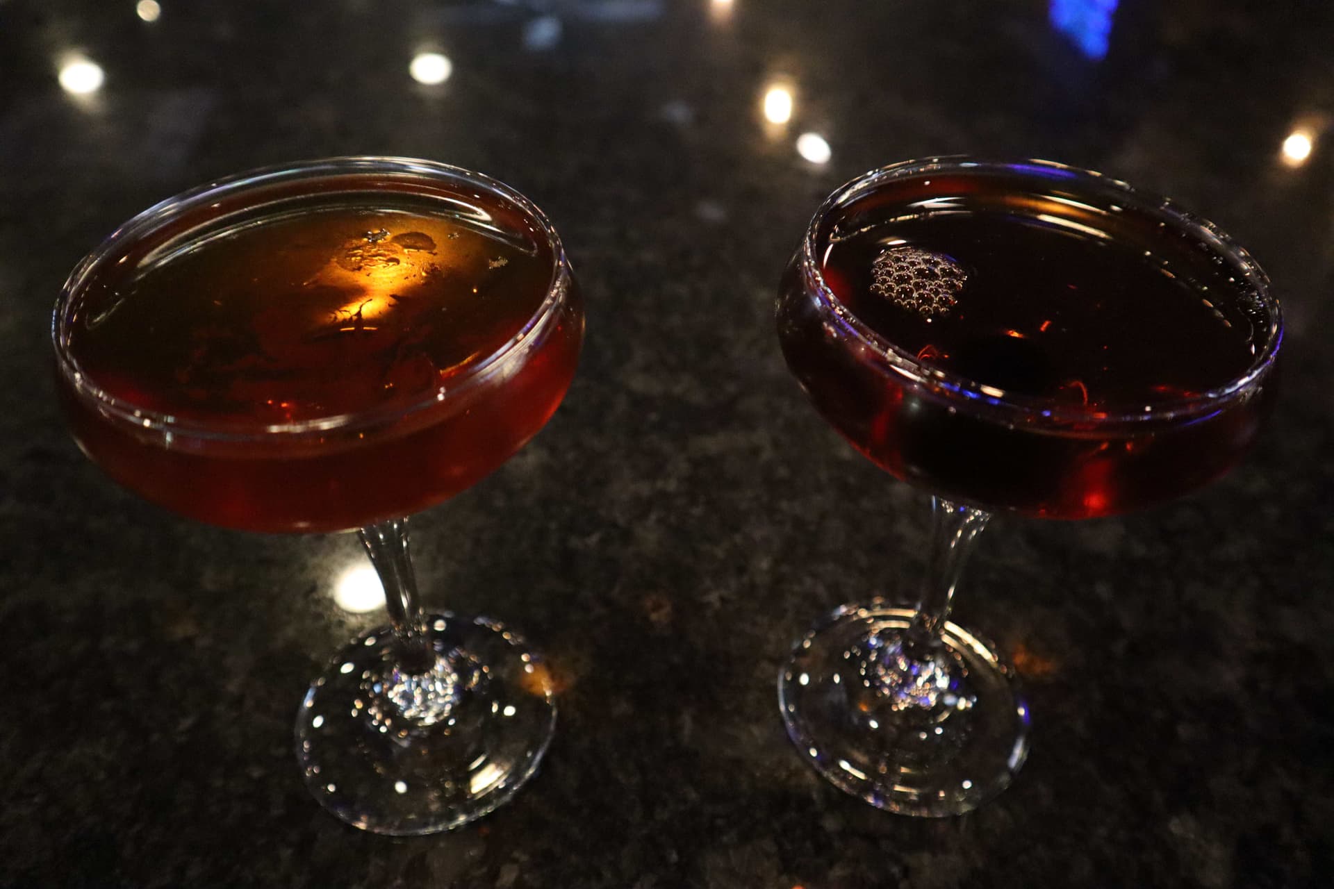 Two Manhattan cocktails on the dark reflective bar top