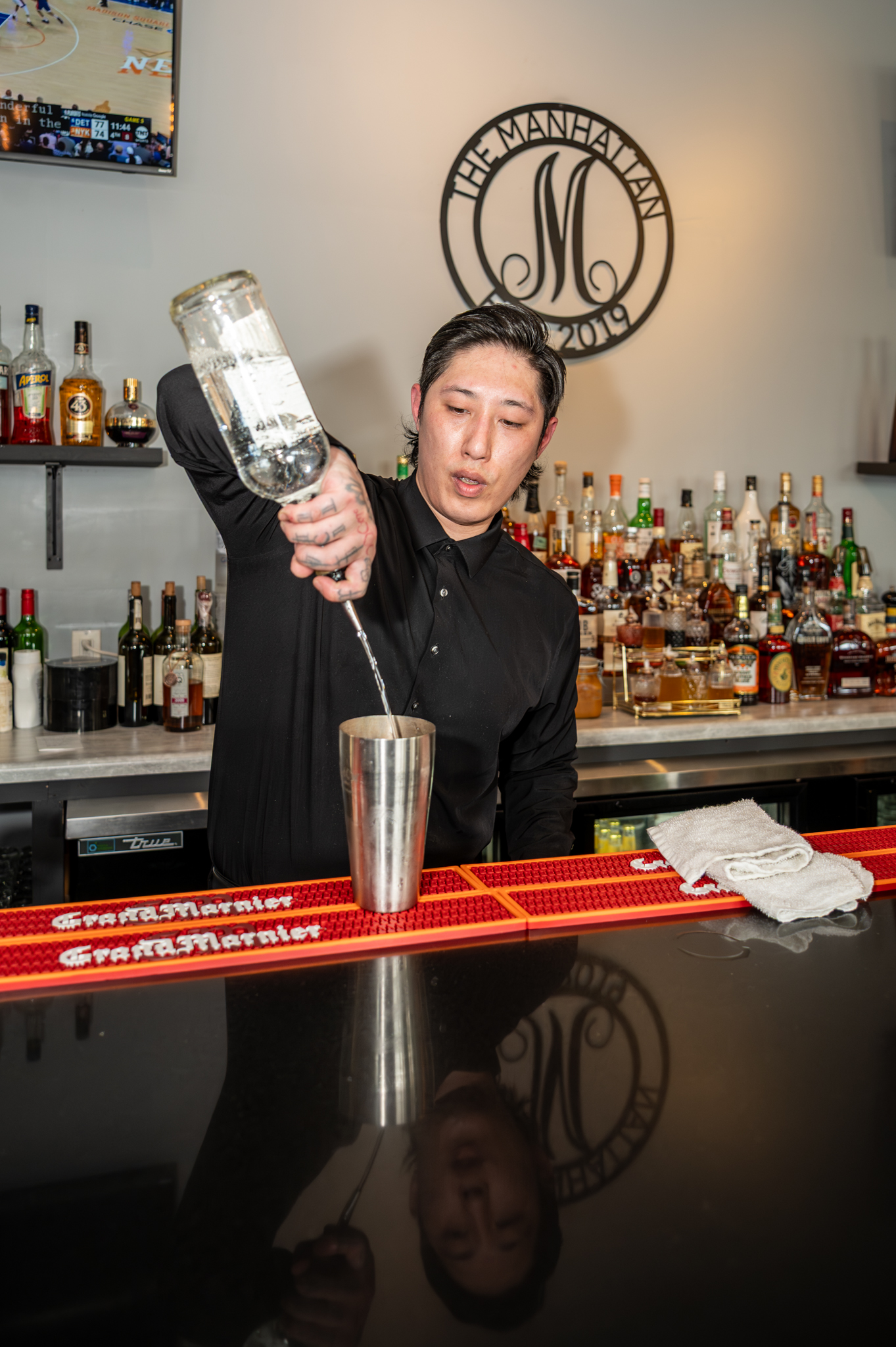 Bartender mixing a cocktail at The Manhattan bar with The Manhattan Est. 2019 sign