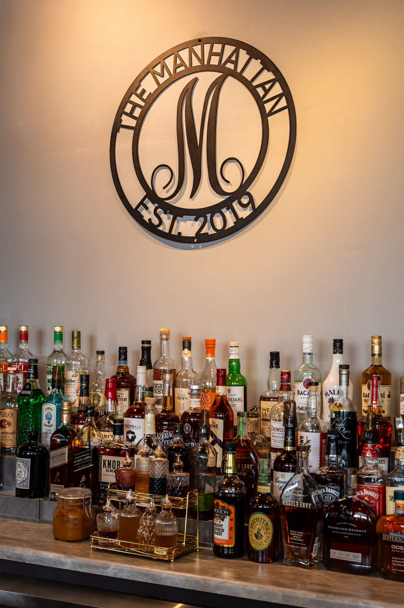 The Manhattan Est. 2019 emblem and curated spirits collection